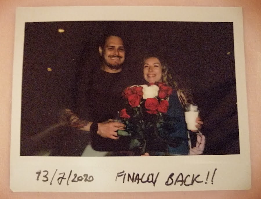 A polaroid picture of Holly holding a bouquet of roses standing smiling next to her boyfriend with the caption "Finally back!"